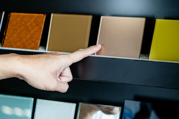 Wall Mural - Architect hand choosing and pointing at beige lacquered glass tile on material samples shelf display in the material library. Colorful acrylic sheet collection for interior finishing idea