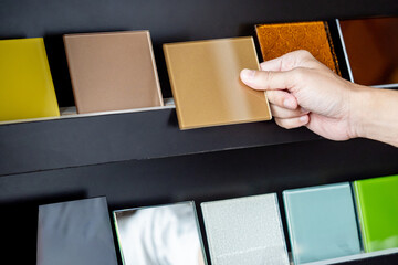 architect hand choosing and picking at beige lacquered glass tile on material samples shelf display 