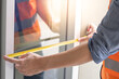 © Summer Paradive - Male worker hands using tape measure checking dimension on aluminum window frame at construction site. Work tool for measurement and installation