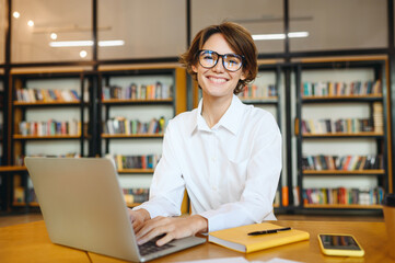 Wall Mural - Young confident happy successful employee IT business woman wear white shirt casual clothes glasses hold use work on laptop pc computer surfing internet sit at office desk. Achievement career concept.