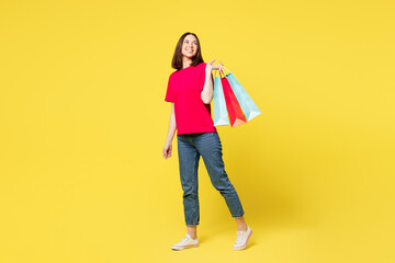 Wall Mural - Full body young happy shocked woman wears pink casual clothes hold in hand paper package bags after shopping walk go look aside isolated on plain yellow background. Black Friday sale buy day concept.