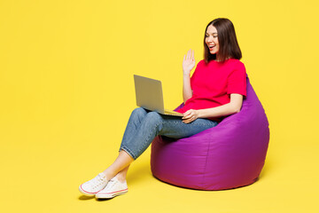 Sticker - Full body young IT woman wear pink t-shirt casual clothes sit in bag chair hold use work on laptop pc computer waving hand isolated on plain yellow orange background studio portrait Lifestyle concept