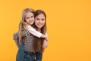 Wall Mural - Portrait of cute little sisters on orange background, space for text