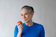© Westend61 - Smiling senior woman holding apple in front of wall