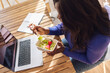 © Westend61 - Woman freelancer eating fruit salad and working on laptop at home