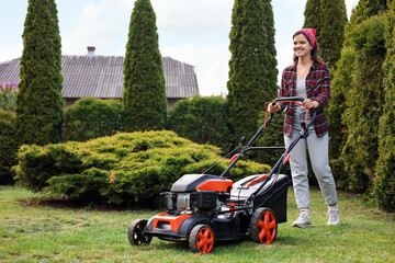 Wall Mural - Smiling woman cutting green grass with lawn mower in garden