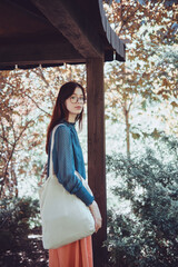 Wall Mural - Teenage girl with a tote bag standing in a wooden garden archway, surrounded by greenery. Stylish and eco-friendly lifestyle portrait. Sustainable living and nature connection concept.