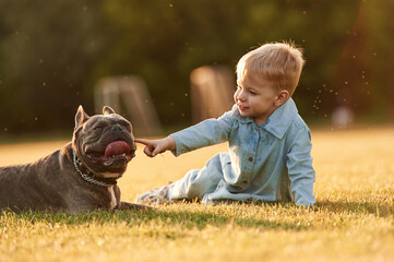 Sitting on the ground. Cute little boy is with dog on the field