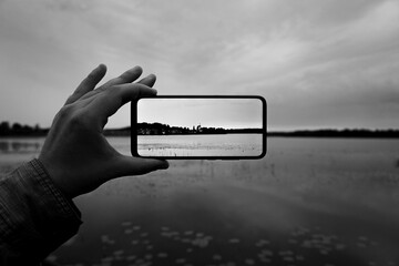 Wall Mural - Cropped hand holding a mobile phone while photographing a lake