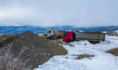 Two dump trucks sparked near quarry against snowy mountains