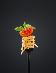 Wall Mural - Spaghetti on a black fork with a piece of tomato, sauce and basil on a dark background. Italian cuisine advertising banner concept.