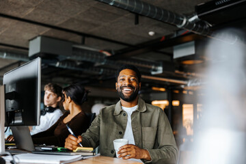 Portrait of happy male entrepreneur sitting at desk in tech start up office