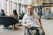© Maskot - Portrait of happy businessman with disability holding coffee cup while sitting on wheelchair at convention center