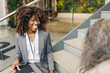 © Maskot - Happy female entrepreneur with curly hair sitting on steps while talking to delegate at convention center
