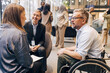 © Maskot - Male entrepreneur sitting on wheelchair and discussing with delegates at convention center