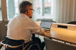 © Maskot - Rear view of male entrepreneur with disability working on laptop at desk