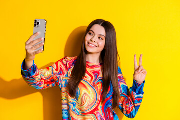 Poster - Photo portrait of lovely young lady take selfie photo v-sign dressed stylish colorful garment isolated on yellow color background