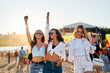 © artiemedvedev - Young women dance at sunset on sandy shore, enjoying music festival. Friends celebrate, summer beach party vibe, arms uplifted in joy. Casual fashion, sea backdrop, golden hour light at music event.