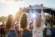 © artiemedvedev - Group of girls at a beach music festival, holding drinks up, enjoying the sunset. Party atmosphere with lively crowd, outdoor event. Female friends celebrate, dance near stage, summer vibes.