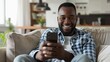 © Bijac - smiling africanamerican man using smartphone on couch at home candid lifestyle photo