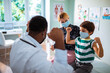 © Marko Geber - Young boy flexing muscles with pediatrician at clinic with mother watching