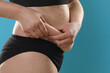 © New Africa - Woman touching belly fat on light blue background, closeup. Overweight problem