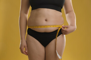 Wall Mural - Woman measuring belly with tape on goldenrod background, closeup. Overweight problem