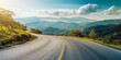 © kiimoshi - The image shows a road with a beautiful landscape of mountains and sky with clouds in the background.