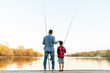 © Богдан Маліцький - african american father and son fishing in the lake and sitting on wooden pier and holding fishing rod outdoors in summer, man teaches child to fish and relax outdoors on river