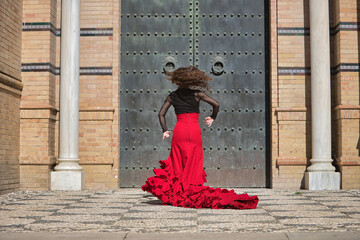 Wall Mural - Young, beautiful, brunette woman in black shirt and red skirt, dancing flamenco in front of an old, black metal door. Flamenco concept, dance, art, typical Spanish.