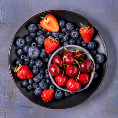 Wall Mural - Top view, extreme close-up, black plate with red cherries, blueberries and strawberries.