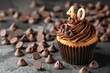 © Ibraheem - A cupcake with a number 40 candle, surrounded by chocolate chips, on a solid dark dark chocolate background.