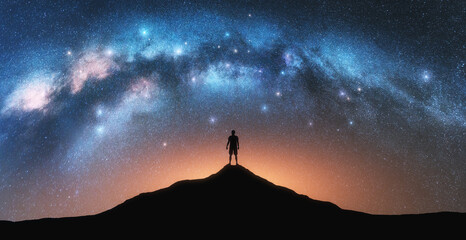 Wall Mural - glowing milky way and man on mountain peak at starry night. silhouette of a guy on the hill, sky wit