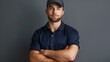 © MD Media - Attractive male service technician worker delivery driver wearing a navy blue polo shirt and hat, standing with his arms crossed on a grey background