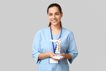 Poster - Portrait of female doctor with spine model on grey background