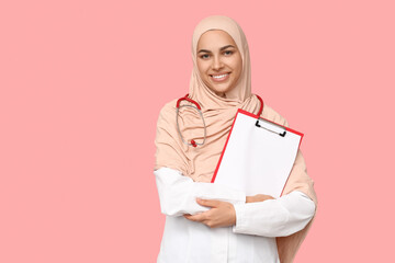 Poster - Portrait of female Muslim doctor holding clipboard with blank paper sheet on pink background