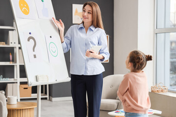 Female psychologist showing pictures on board to little girl in office