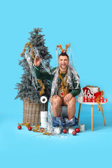 Sticker - Young man sitting on toilet bowl with tinsel and Christmas decor against blue background