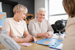 © Pixel-Shot - Happy mature couple with world map planning trip in travel agency