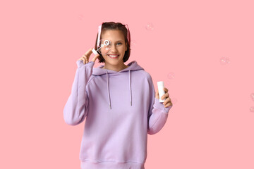 Poster - Happy teenage girl blowing soap bubbles on pink background