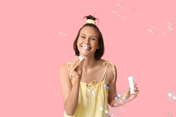 Wall Mural - Teenage girl blowing soap bubbles on pink background