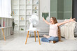 © Pixel-Shot - Young girl sitting on floor in front of electric fan in living room
