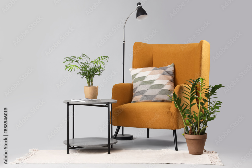 Comfortable armchair with cushion and coffee table with plant on grey background
