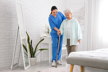 Poster - Physical therapist helping senior woman with stick to walk in bedroom