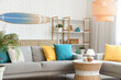 © Pixel-Shot - Light interior of living room with cozy sofa, coffee table, lamp and surfboard