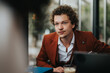 © qunica.com - A young businessman in a red suit is engaged in a serious conversation at a modern cafe, highlighting professional interaction and discussion.