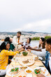 © Xavier Lorenzo - Vertical shot of happy diverse group of friends enjoying dinner barbecue in summer at home terrace. Young people cheering with red wine at bbq party. Food and family moments concept