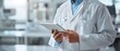© Naret - Doctor in lab coat using digital tablet in modern medical facility, close-up view.