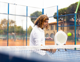 Wall Mural - Focused middle-aged Latin man padel player hitting ball with racket on hard court in summer