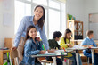 © Home-stock - Cheerful young female teacher working in elementary school, happy teacher and girl smiling at camera in classroom interior